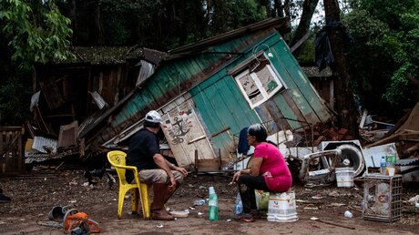Menschen sitzen vor einer von Überschwemmungen zerstörten Hütte. Die Zahl der Toten nach den schweren Unwettern im Süden Brasiliens ist weiter gestiegen. / © ---/XinHua (dpa)