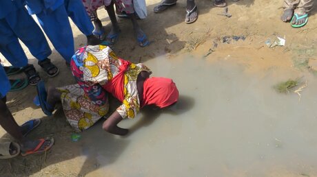 Ein durstiges Mädchen trinkt in Maiduguri, Nigeria, aus einer verdreckten Pfütze. Sauberes Trinkwasser gibt es nicht mehr. / © Sam Olukoya (dpa)