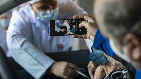 Brasilien: Ein Mann fotografiert mit dem Handy, wie seiner Mutter im Auto eine Covid-19-Impfung mit dem Impfstoff der chinesischen Firma Sinovac verabreicht wird. / © Andre Penner/AP (dpa)