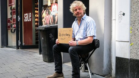 Der Fotograf Harald Oppitz schlüpft in Bonn in die Rolle eines Bettlers und hält ein Pappschild. / © Klaus Dieter Warnke (KNA)