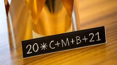 Ein Aufkleber mit der Aufschrift "20*C+M+B+21" liegt neben einer Krone / © Sina Schuldt (dpa)