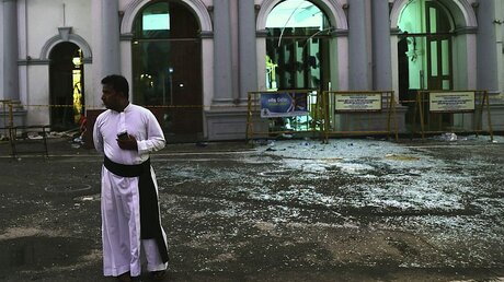 Ein katholischer Priester aus Sri Lanka steht neben Glasscherben vor der Kirche St. Anthony's. / © Manish Swarup (dpa)