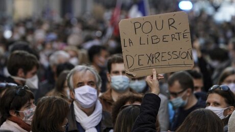 Ein Protestteilnehmer in Lyon hält ein Plakat hoch, auf dem zu lesen ist (Pour la liberté d'expression) "Für die Redefreiheit". / © Laurent Cipriani/AP (dpa)