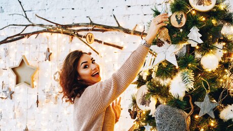 Eine Frau schmückt einen Weihnachtsbaum / © GaudiLab (shutterstock)