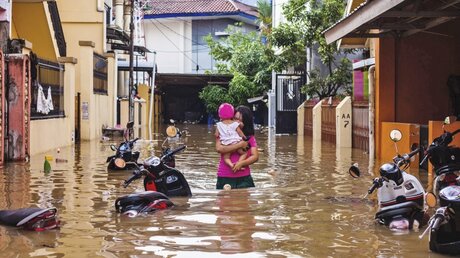 Eine Frau trägt ihre Tochter durch ein überschwemmte Viertel auf der indonesischen Insel  / © Yusuf Wahil (dpa)