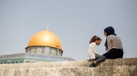 Eine muslimische Frau und ein Mädchen sitzen auf einer Mauer vor der Al-Aksa-Moschee (Al-Aqsa-Moschee) und dem Felsendom auf dem Tempelberg in der Altstadt von Jerusalem / © Corinna Kern (KNA)