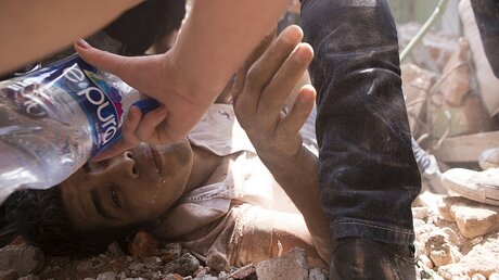 Ein Mann, der nach dem Erdbeben inmitten der Trümmer eines Gebäudes liegt, wird mit Trinkwasser versorgt / © Pablo Ramos (dpa)