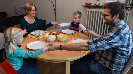 Vater, Mutter und Kinder reichen sich die Hände und beten vor dem Essen.  / © Harald Oppitz (KNA)