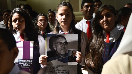 Eine junge Gläubige hält während einer Messe ein Bild des Bischofs Oscar Romero. / © Vladimir Chicas (dpa)
