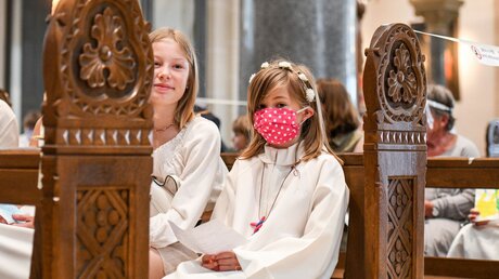 Ein Mädchen sitzt mit Mundschutz in einer Kirchenbank bei der Messe zur Feier der Erstkommunion / © Harald Oppitz (KNA)