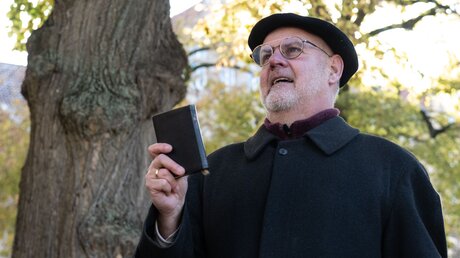 Der ehemalige Pastor Harald Storz hält an der St.-Albani-Kirche eine alte Bibel, die nicht mehr gebraucht wird / © Swen Pförtner (dpa)