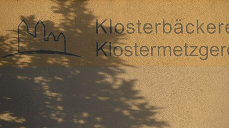 Ein Baum wirft am 11. Oktober 2023 einen Schatten auf den Schriftzug der Klostermetzgerei an einer Hauswand der Abtei Münsterschwarzach in Schwarzach / © Harald Oppitz (KNA)