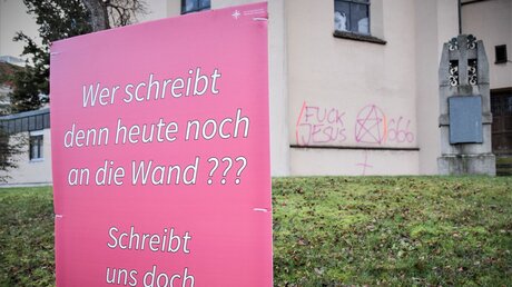 Rosa Schild mit Aufschrift vor einer mit Graffiti beschmierten Hauswand in Augsburg. 
 / © Christopher Beschnitt (KNA)