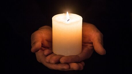 Hände halten eine brennende weiße Kerze / © Corinne Simon (KNA)