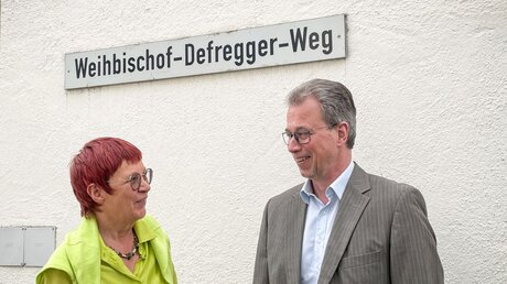 Die Historikerin Marita Krauss (l.) und Rainer Schnitzler, Bürgermeister von Pöcking, vor dem Straßenschild des Weihbischof-Defregger-Wegs. / © Christoph Renzikowski (KNA)