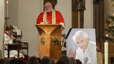 Erzbischof Reinhard Kardinal Marx spricht im Münchner Liebfrauendom während der Silvestermesse neben einem Foto des verstorbenen emeritierten Papstes Benedikt XVI.  / © Lennart Preiss (dpa)