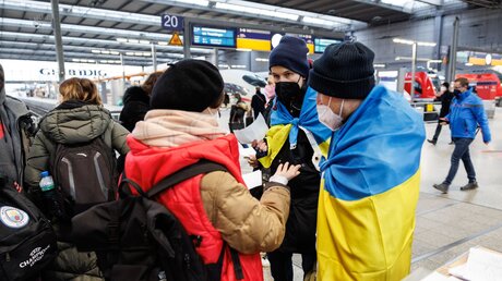 Zwei ukrainisch sprechende Helfer (r) sprechen an einem Info-Point am Münchner Hauptbahnhof für geflüchtete Ukrainer mit einer Frau aus der Ukraine / © Matthias Balk (dpa)