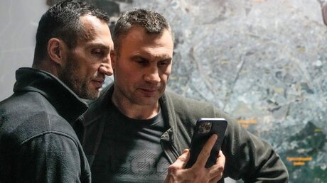 Vitali Klitschko (r), Bürgermeister von Kiew und ehemaliger Box-Profi, und sein Bruder Wladimir Klitschko, ebenfalls ehemaliger Box-Profi, schauen auf ein Smartphone im Rathaus in Kiew / © Efrem Lukatsky (dpa)