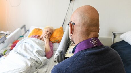 Ein Seelsorger sitzt am Krankenbett und spricht mit einer Frau auf der Palliativstation in der Universitätsklinik Bonn / © Harald Oppitz (KNA)