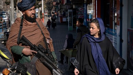Kabul: Ein Taliban-Kämpfer steht Wache, während eine Frau vorbeiläuft / © Ebrahim Noroozi/AP (dpa)