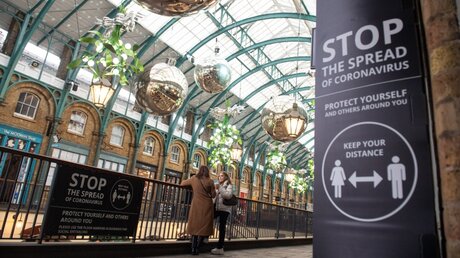London: Zwei Frauen stehen im Covent Garden neben Corona-Warnhinweisen / © Dominic Lipinski (dpa)