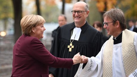 Martin Dutzmann (M) und Prälat Karl Jüsten (r) empfangen Angela Merkel zum ökumenischen Gottesdienst / © Britta Pedersen (dpa)