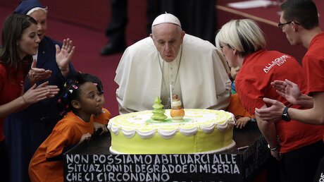 Papst Franziskus pustet eine Kerze auf einer Torte am Abend vor seinem 82. Geburtstag in der Vatikanischen Audienzhalle aus. / © Gregorio Borgia (dpa)