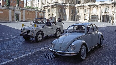 Papst Johannes Paul II. fährt am 26. Mai 2004 im Vatikan im Papamobil an dem letzten jemals gebauten VW-Käfer vorbei, der ihm zwei Tage vorher überreicht wurde / © Osservatore Romano (KNA)