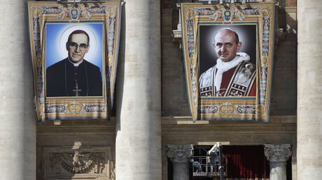 Porträts von Erzbischof Oscar Romero (l) und Papst Paul VI. am Petersdom / © Alessandra Tarantino (dpa)