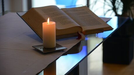Leuchtende Kerze neben einer Bibel (KNA)