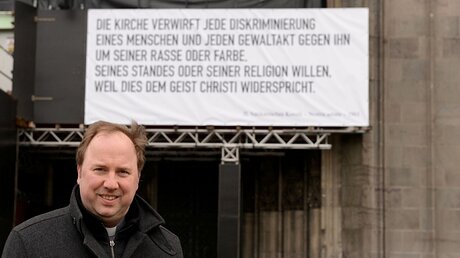 Msgr. Kleine mit Domplakat gegen Diskriminierung  / © Mira Unkelbach (Dombauhütte Köln)