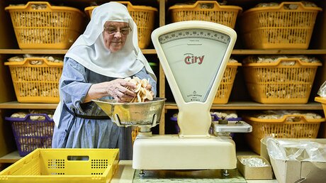 Schwester Theresia Kucklick wiegt Hostien auf einer alten Waage und verpackt sie in Plastikbeuteln / © Jannis Chavakis (KNA)