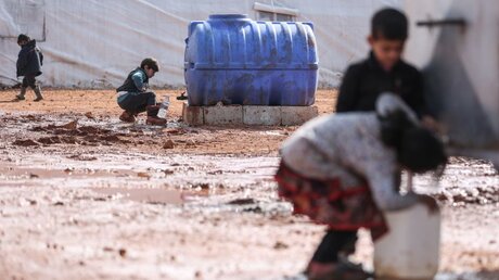 Syrien: Kinder füllen in einem provisorischen Lager für Familien Behälter mit Wasser auf / © Anas Alkharboutli (dpa)