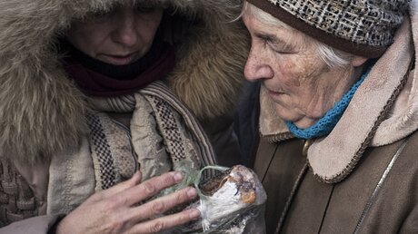 Zwei ältere Frauen, Einwohnerinnen von Awdijiwka, halten gefrorenen Fisch in den Händen. / © Evgeniy Maloletka (dpa)