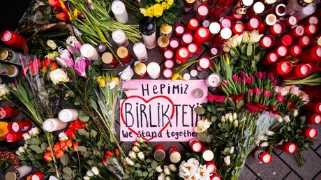 "We stand together": Zwischen den niedergelegten Blumen am Tatort in Hanau liegt eine Anteilsbekundung / © Andreas Arnold (dpa)