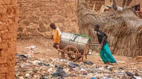 Zwei Jungen in Burkina Faso transportieren eine Tonne mit Wasser / © MattLphotography (shutterstock)