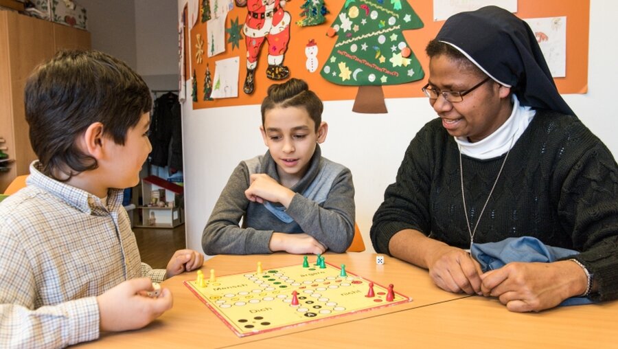 Caritas-Sozialzentrum: zwei Jungen und eine Ordensschwester spielen Mensch-ärgere-dich-nicht / © Elisabeth Schomaker (KNA)