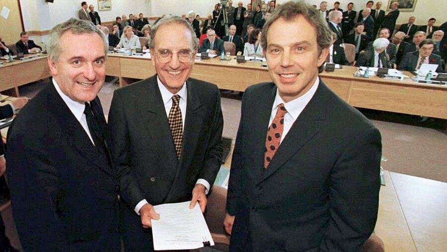 Der britische Premierminister Tony Blair (r-l), US Senator George Mitchell, und der irische Premierminister Bertie Ahern lächeln nach der Unterzeichnung des Friedensabkommens / © Dan_Chung_Pool (dpa)