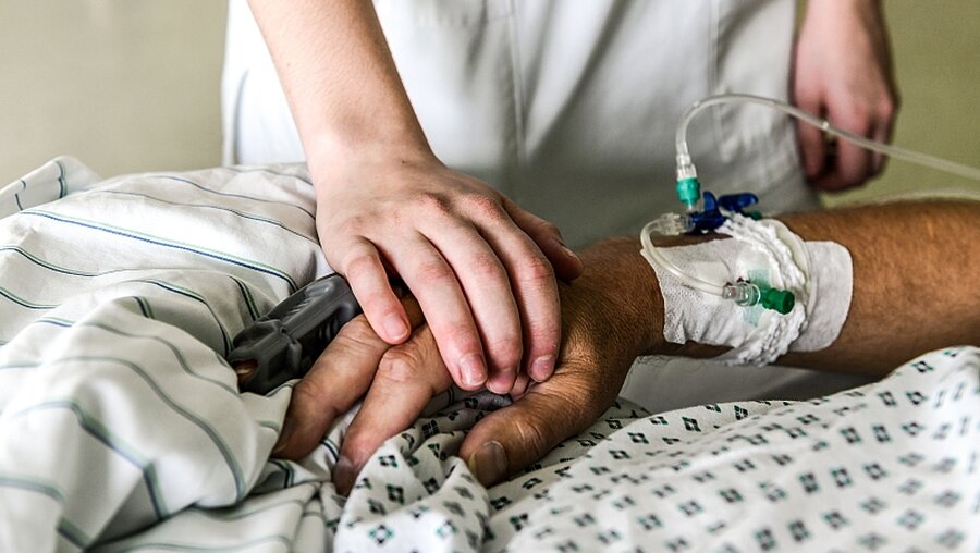 Die Hand einer Pflegerin liegt auf dem Handrücken eines Patienten auf der Intensivstation im Cura Krankenhaus Bad Honnef. / ©  Harald Oppitz (KNA)