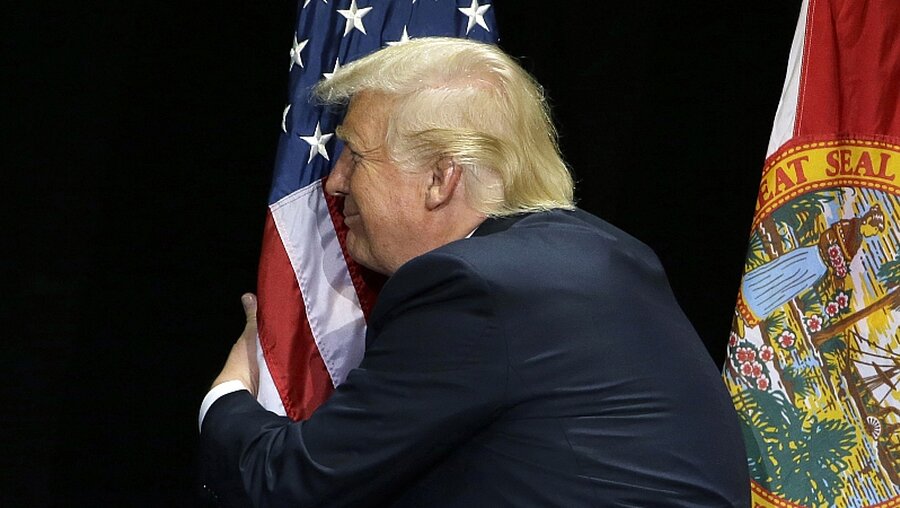 Donald Trump umarmt US-Flagge / © Chris O'meara (dpa)