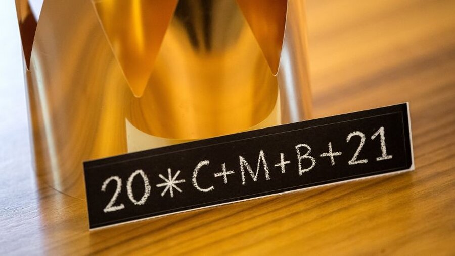 Ein Aufkleber mit der Aufschrift "20*C+M+B+21" liegt neben einer Krone / © Sina Schuldt (dpa)