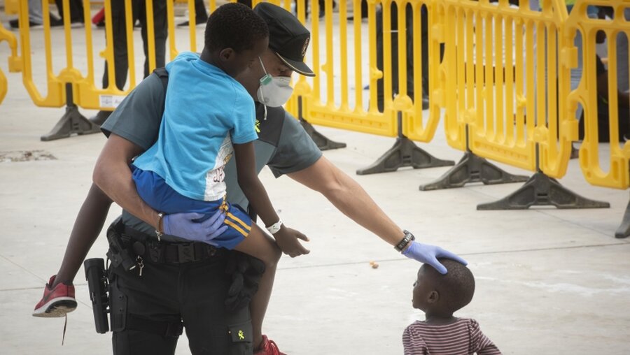 Ein Beamter der Guardia Civil trägt ein Flüchtlingskind in einem Sportzentrum in Los Barrios / © Marcos Moreno (dpa)