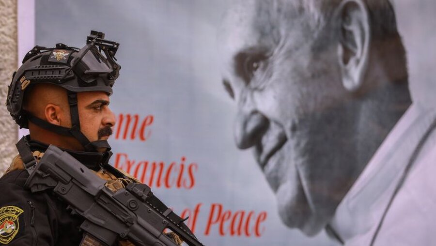 Ein bewaffneter Polizist steht an einer Kirche neben einem Bild des Papstes inmitten einer Sicherheitskontrolle / © Ameer Al Mohammedaw (dpa)