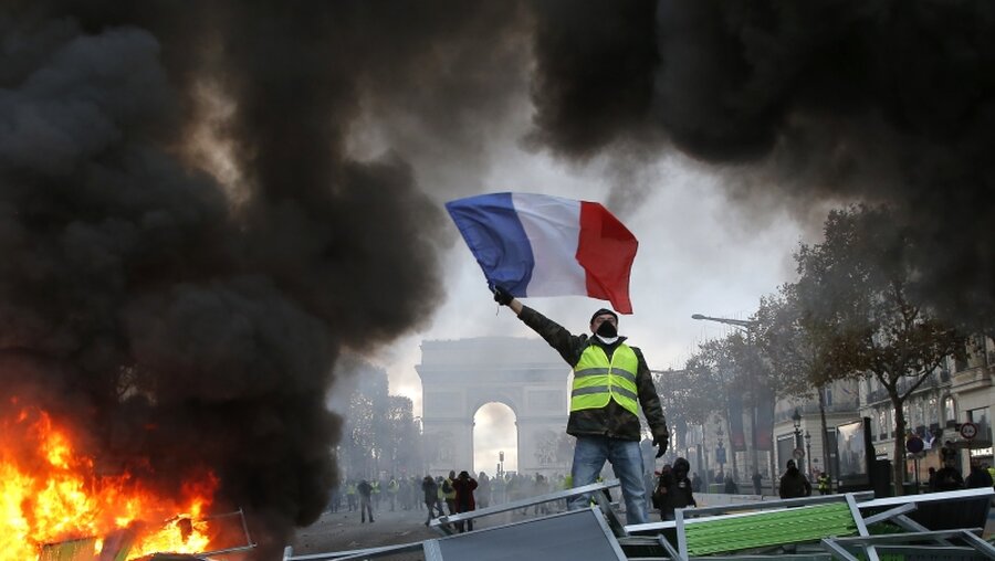 Ein Demonstrant mit einer gelben Weste schwenkt die französische Flagge / © Michel Euler (dpa)