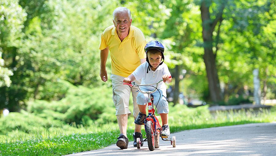 Ein Großvater bringt seinem Enkel das Fahrrad fahren bei. / © dotshock (shutterstock)