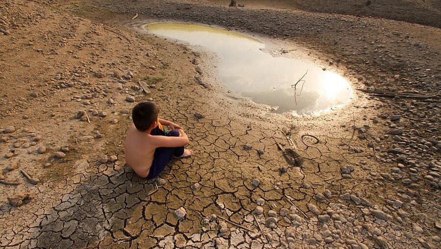 Ein Junge sitzt vor einer austrocknenden Wasserstelle / © Piyaset (shutterstock)
