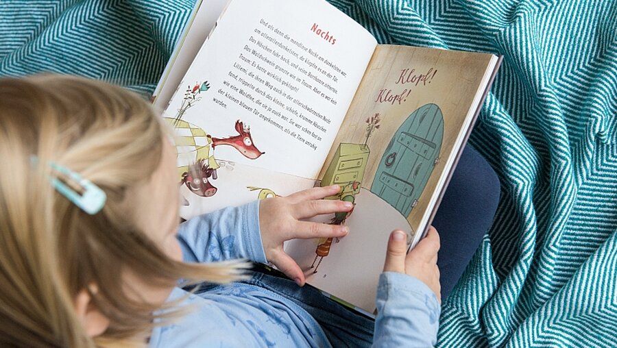  Ein kleines Mädchen liest in einem Buch / © Elisabeth Schomaker (KNA)