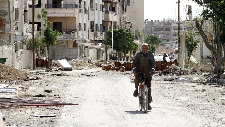 Ein Mann fährt mit seinem Fahrrad durch die zerstörte Stadt Duma / © Hummam Sheikh Ali (dpa)