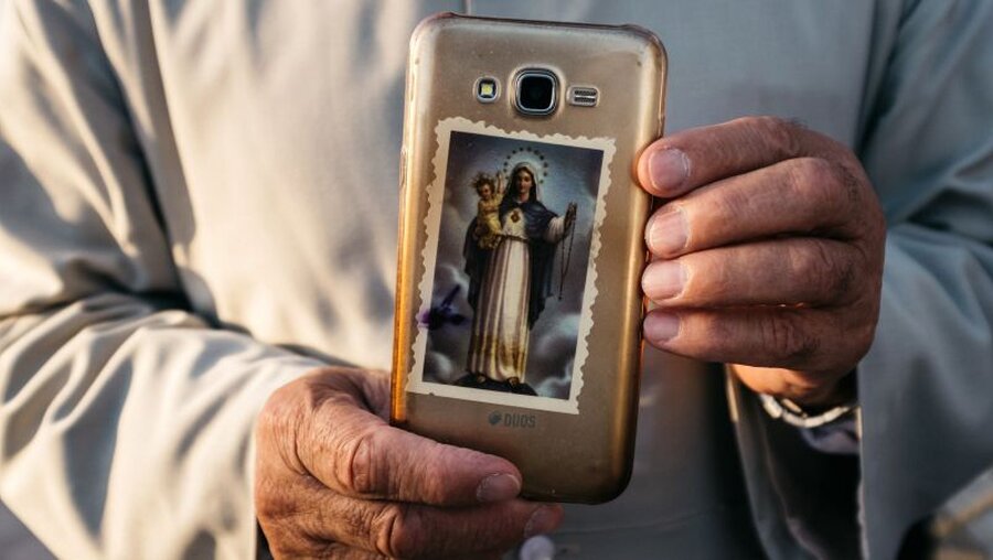 Ein Mann im Irak hält ein Handy mit einem Sticker, der Muttergottes mit Jesuskind zeigt in den Händen / © Jean-Matthieu Gautier (KNA)
