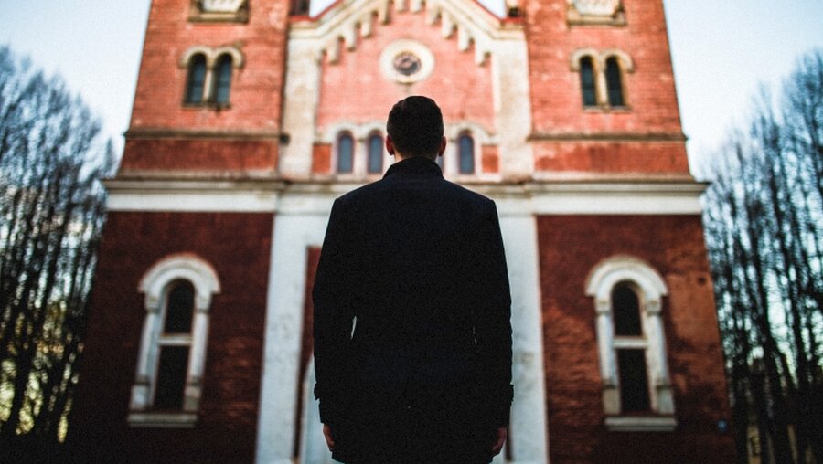 Ein Mann steht vor einer Kirche / © Jurgis Rudaks (shutterstock)